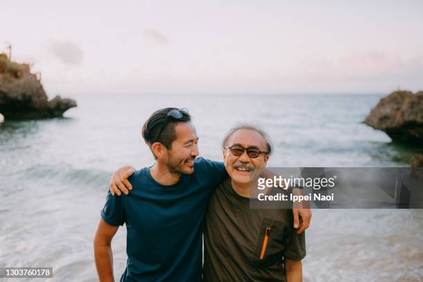 senior father and adult son having a good time on beach at sunset - zoon stockfoto's en -beelden