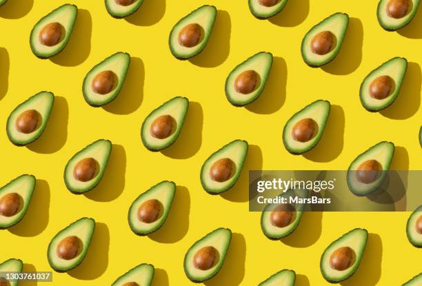l'avocado dimezza il motivo con ombra dura e illuminazione alla moda su sfondo giallo - repetition foto e immagini stock