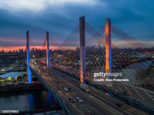 traffic on kosciuszko bridge illuminated at dusk, with the remote view of manhattan and brooklyn over the industrial zone of williamsburg. - kosciuszko bridge stock pictures, royalty-free photos & images