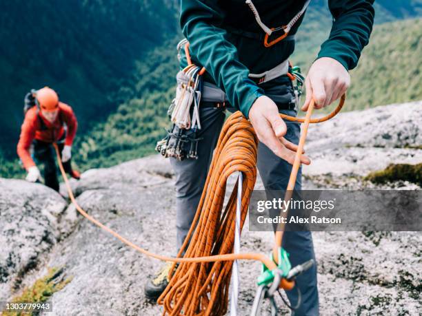 a rock climber belays his climbing partner up to the top of a tall, remote mountain - climbers team stock-fotos und bilder