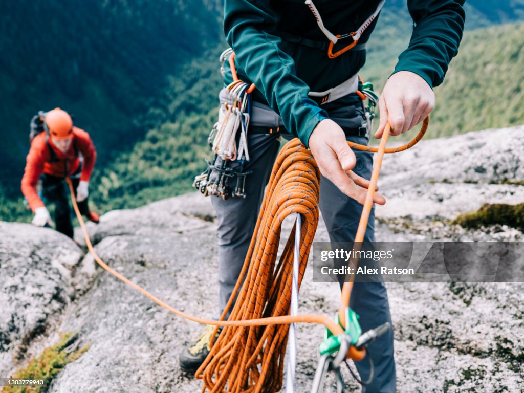 A rock climber belays his climbing partner up to the top of a tall, remote mountain