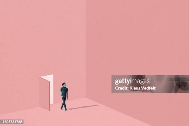 man with legs crossed standing against coral door - access stockfoto's en -beelden