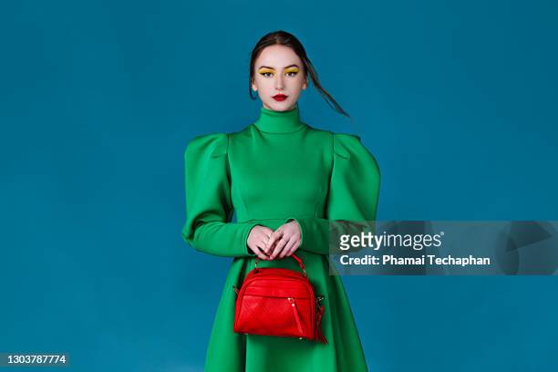 beautiful woman in green dress holding a red handbag - green purse stockfoto's en -beelden