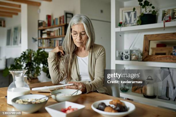 retired woman enjoying leisurely breakfast and newspaper - media breakfast stock pictures, royalty-free photos & images