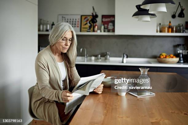 relaxed senior woman reading newspaper over breakfast - media breakfast stock pictures, royalty-free photos & images