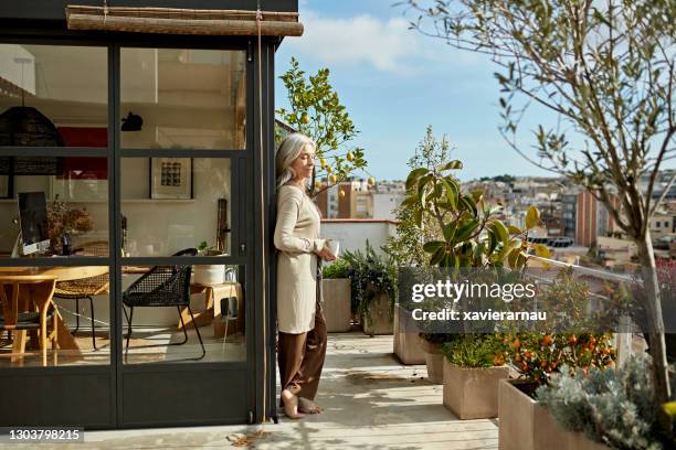 relaxed senior woman standing on sunny deck with coffee - old tree stock pictures, royalty-free photos & images