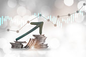 Green arrow upward on stack of coins and growth graph on bokeh background