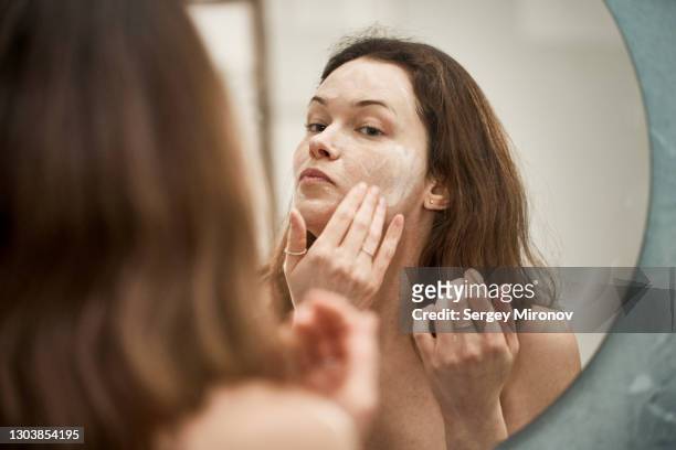 young woman applying wash foam to her face. - woman mirror stockfoto's en -beelden