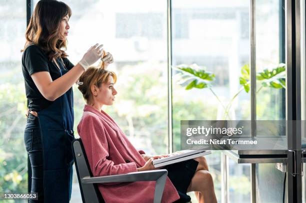 side view of asian hairdresser is dyeing the hair for a female customer in beauty salon. young women having her hair colored at hair salon. - hair salon 個照片及圖片檔