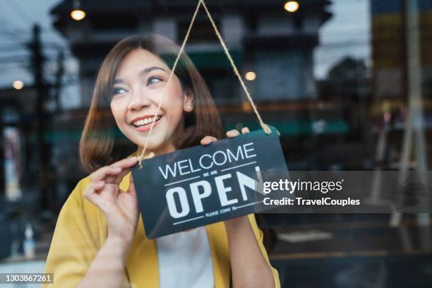 asian woman waitress holding open sign in cafe bar flipping hanging on door window. small business owner and startup with cafe shop. installing open and close label concept - reopening ceremony stockfoto's en -beelden