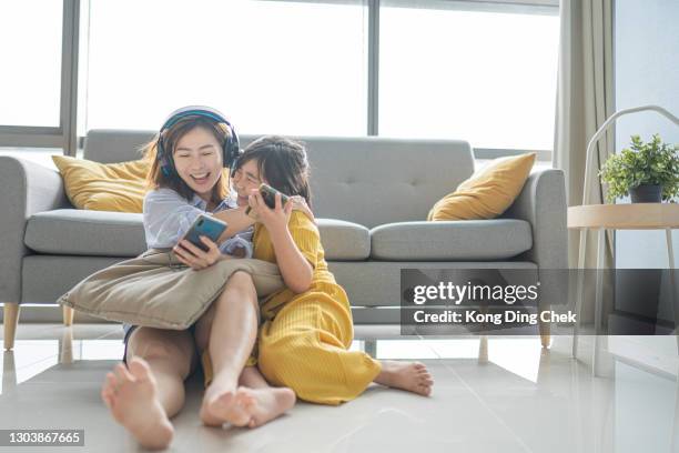 aziatische chinese moeder en dochter die van het binden van tijd in woonkamer genieten die aan muziek met telefoonhoofdtelefoon luisteren - music room stockfoto's en -beelden