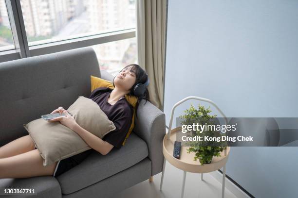 asian chinese teenage girl enjoying listening music at home during weekend on sofa with smart phone and headphone - lying on back girl on the sofa stock pictures, royalty-free photos & images