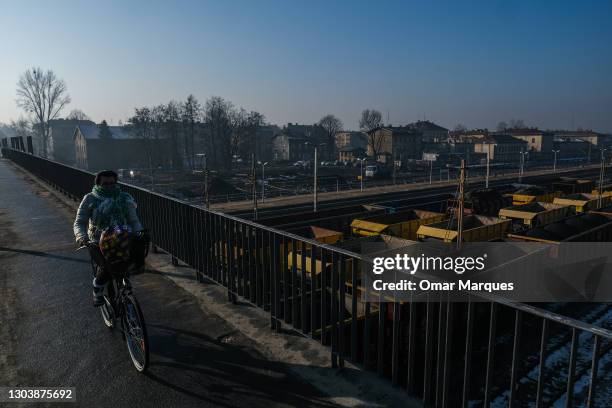 Woman rides a bicycle on a bridge above open freight wagons full of coal during a day that the level of PM2.5 dust concentration amounted to 198...