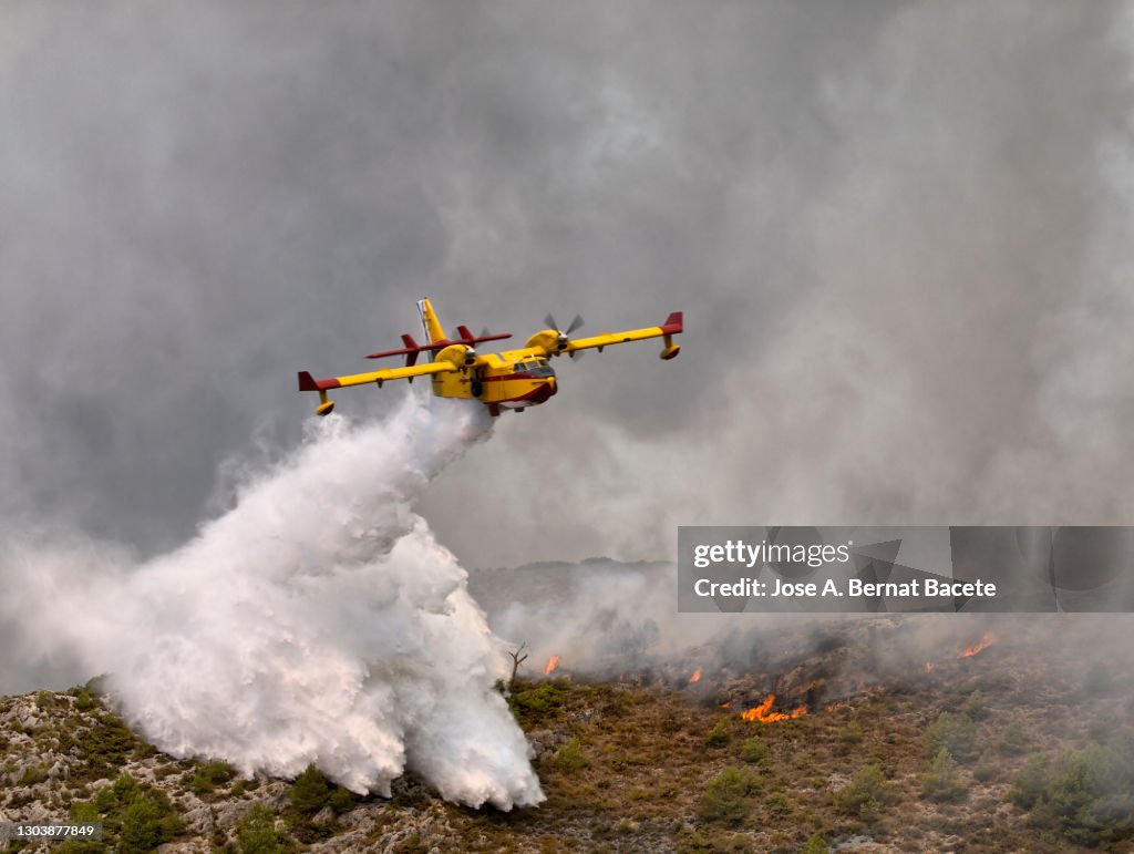 Fire-fighting plane discharging water over a burning forest in a forest fire.