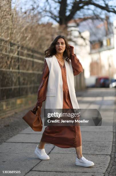 Masha Sedgwick wearing Envelope 1976 brown dress, Polene beige bag, Zara beige vest, Copenhagen Studios white sneaker on February 22, 2021 in Berlin,...