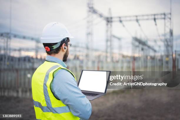 portrait of confident male engineer using a laptop in front of electric power station. - electricity pylon imagens e fotografias de stock