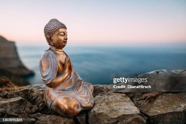 figure de bouddha se reposant sur un rocher devant des montagnes et la mer méditerranée sur majorque pendant le coucher du soleil - tibet stock photos et images de collection