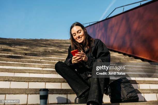 woman sitting on stairs and texting on her smartphone - disinvolto foto e immagini stock