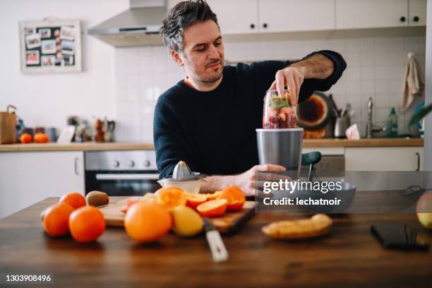 自宅で朝食にフルーツスムージーを準備している男性 - ミキサー ストックフォトと画像