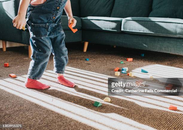 child stands on carpet in front of a corner sofa. wooden building blocks are scattered over the floor. - lekrum bildbanksfoton och bilder