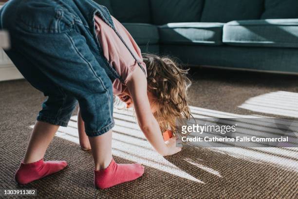 little girl bends over and touches the floor, smiling through her little legs - leg stretch girl stock pictures, royalty-free photos & images