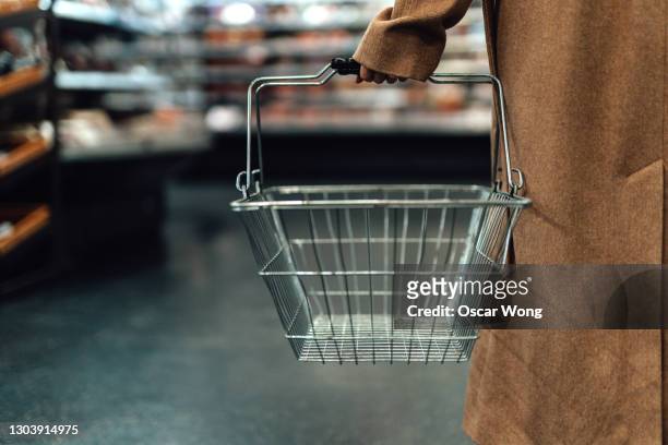 woman carrying empty shopping basket in supermarket - consumerism stockfoto's en -beelden
