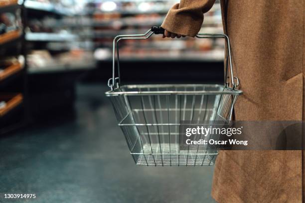 woman carrying empty shopping basket in supermarket - consumerism imagens e fotografias de stock