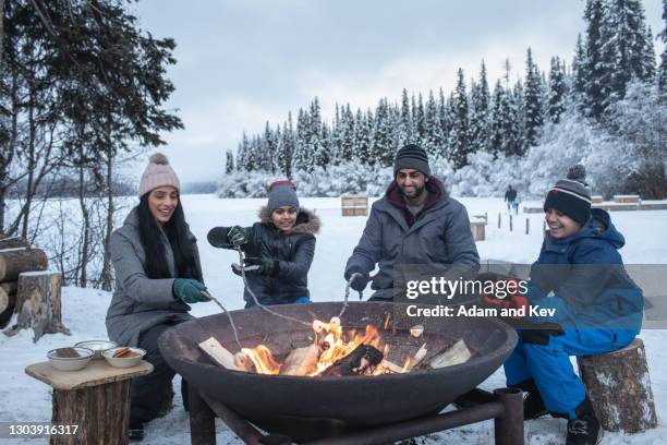 family of four roast marshmallows over open fire in wintery setting - fun lovers unite stock pictures, royalty-free photos & images