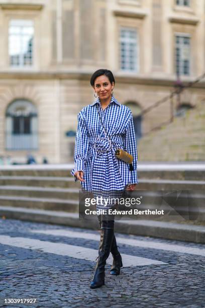 Adriana Seminario wears earrings, a blue and white checked pattern printed dress from Marques Almeida, a golden metallic Saint-Laurent YSL bag, thigh...