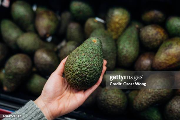 woman choosing avocados in supermarket - avocado stock-fotos und bilder