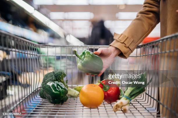 woman put down green pepper in shopping trolley at supermarket - picking up groceries stock pictures, royalty-free photos & images