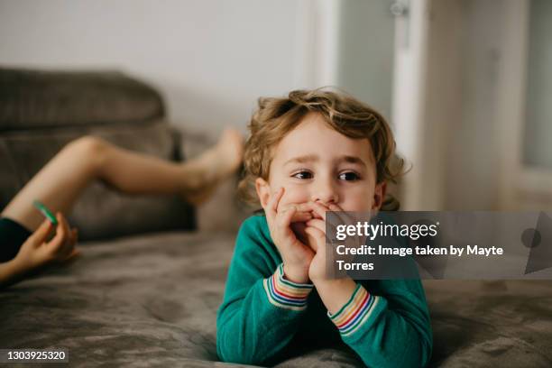 boy in sofa watching tv with brother's legs behind him - boy curly blonde stock pictures, royalty-free photos & images