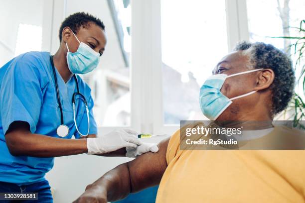 african american nurse injecting a vaccine to a senior man - black people wearing masks stock pictures, royalty-free photos & images