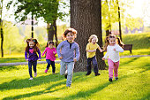 many young children smiling running along the grass in the park