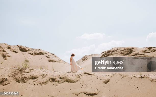 schöne junge frau trägt ein offenes rückenkleid walking in einer wüste - beige stock-fotos und bilder
