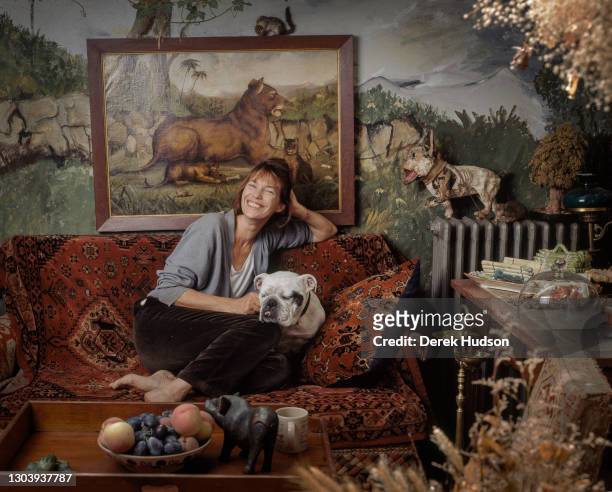 Jane Mallory Birkin, OBE poses barefoot on a sofa covered with an oriental woven carpet with her British Bulldog Dora by her side in the salon of her...