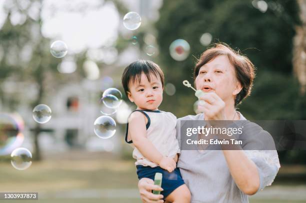 asiatische chinesische großmutter spielen blase zusammen mit ihrem enkel in öffentlichen park am wochenende abend hinterleuchtet - asian granny pics stock-fotos und bilder