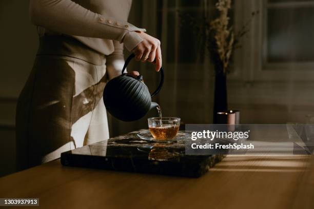 mulher anônima curtindo uma tarde lenta, cuidadosamente derramando-se chá - folhas de chá - fotografias e filmes do acervo