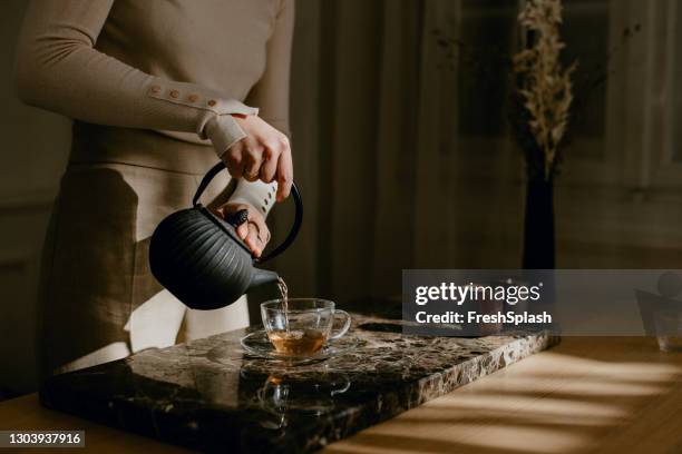 mujer anónima disfrutando de una tarde lenta, vertiéndose cuidadosamente té - tea leaves fotografías e imágenes de stock