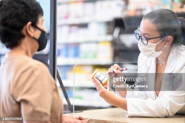 female pharmacist wearing a face mask while speaking to a customer stock photo - pharmacy mask stock pictures, royalty-free photos & images