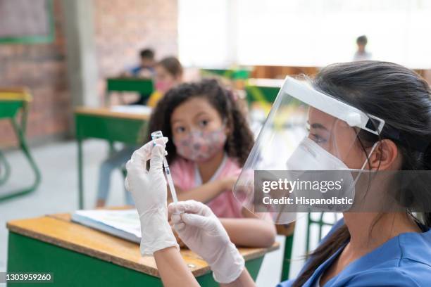 nurse preparing a covid-19 vaccine for a girl at school - global health stock pictures, royalty-free photos & images