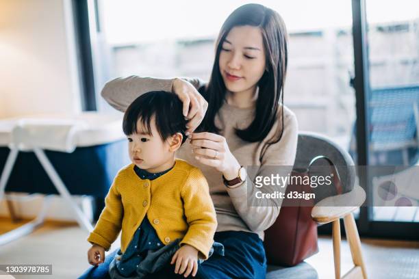 young asian mother tying hair of little daughter and getting dressed at home before heading out. family lifestyle - japanese mom stock pictures, royalty-free photos & images