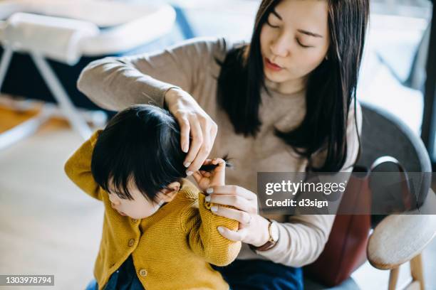 young asian mother tying hair of little daughter and getting dressed at home before heading out. family lifestyle - beautiful hair at home stock-fotos und bilder