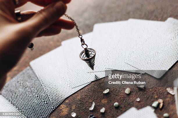 a hand holds an iron pendulum over laid out tarot cards - divination stockfoto's en -beelden