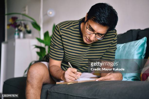 man writing in a diary sitting on a sofa - tagebuch stock-fotos und bilder