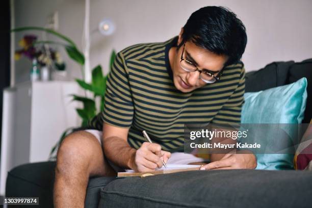 man writing in a diary sitting on a sofa - writing activity stock pictures, royalty-free photos & images