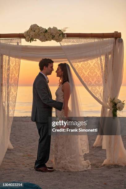 bride and groom facing each other in silhouette, under chupah, on beach with sunset in background - sunset beach bouquet wedding couple stock pictures, royalty-free photos & images