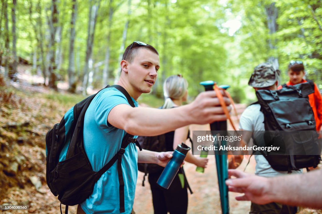 Smiling Hiker Passing Poles To Friend While Drinking Water