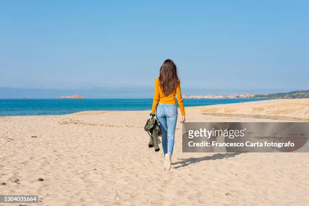 young adult woman strolling on beach - jeans back stockfoto's en -beelden