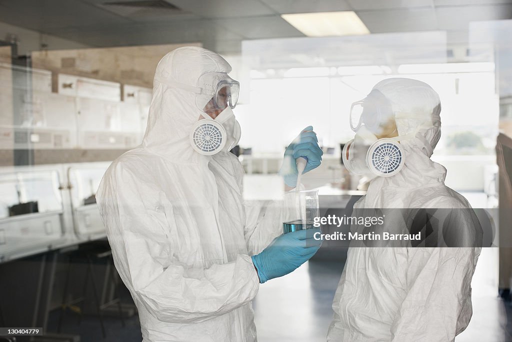 Scientists in protective gear putting liquid in beaker in lab